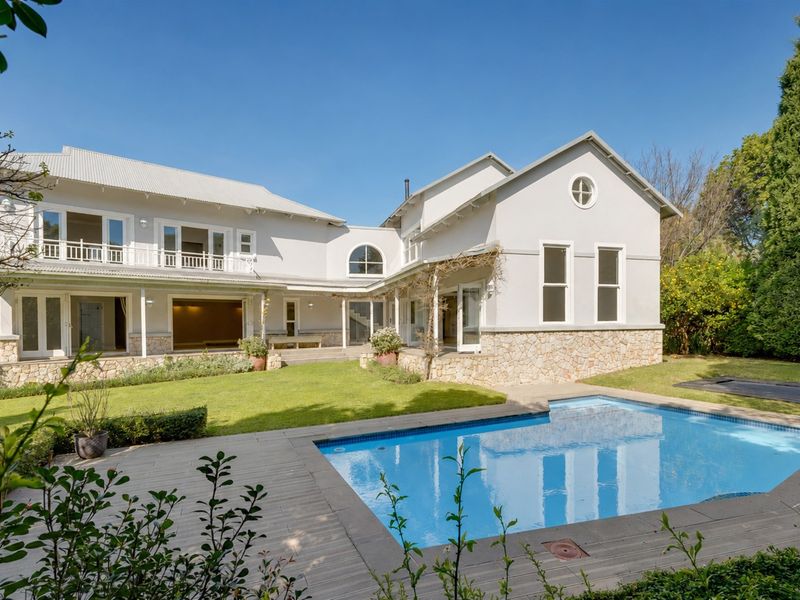 Rear view of a spacious two-story house featuring a swimming pool, stone-clad base, metal roof, and a well-maintained garden with a deck area.