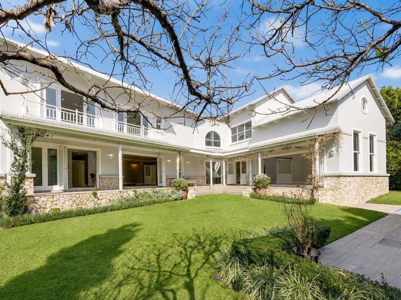Spacious rear elevation featuring a covered patio, balcony, stone cladding, and a well-maintained garden with a swimming pool.