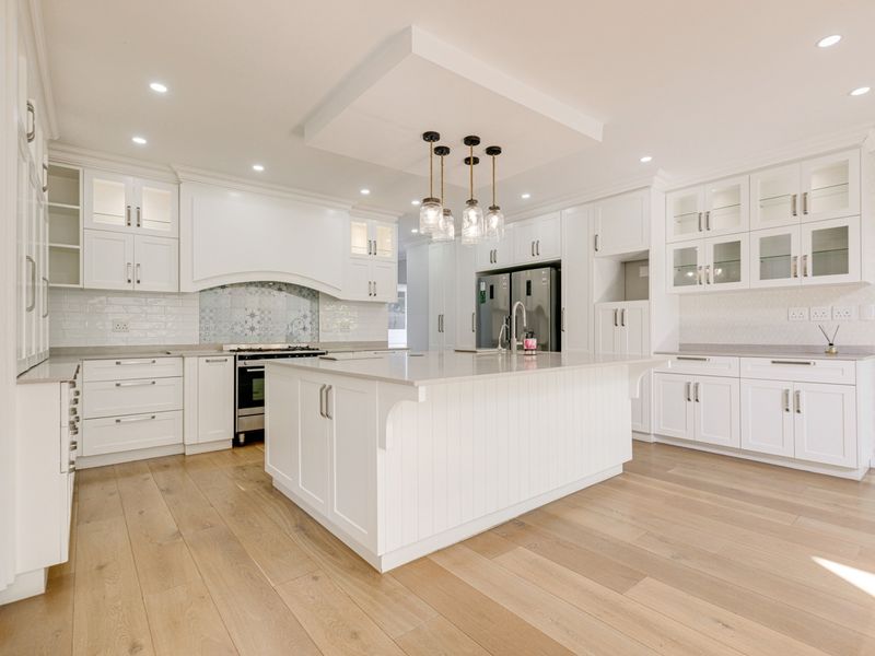 Modern, bright kitchen featuring white shaker cabinetry, a large central island with quartz countertops, subway tile backsplash, and high-quality engineered wood flooring.