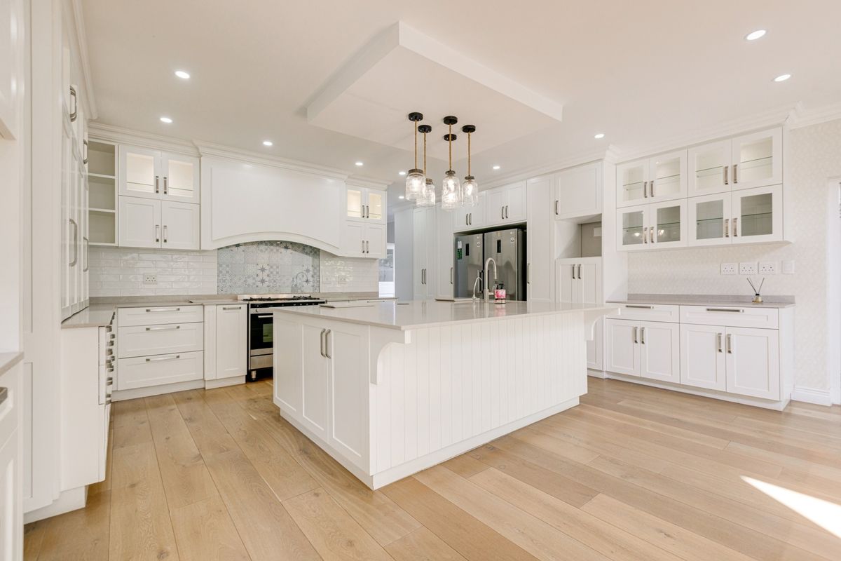 Modern, bright kitchen featuring white shaker cabinetry, a large central island with quartz countertops, subway tile backsplash, and high-quality engineered wood flooring.