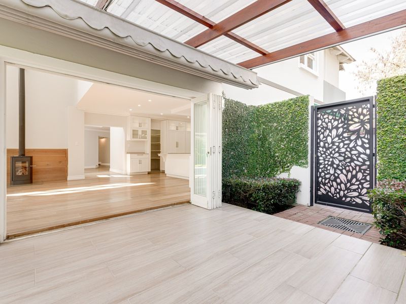 A covered patio featuring tiled flooring, a timber pergola, and folding glass doors that open into a bright, open-plan living and kitchen area.