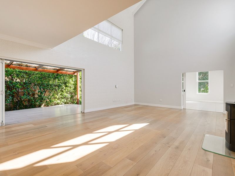 Spacious living area featuring high vaulted ceilings, light hardwood flooring, a modern freestanding fireplace, and large bi-fold doors opening to a covered patio.