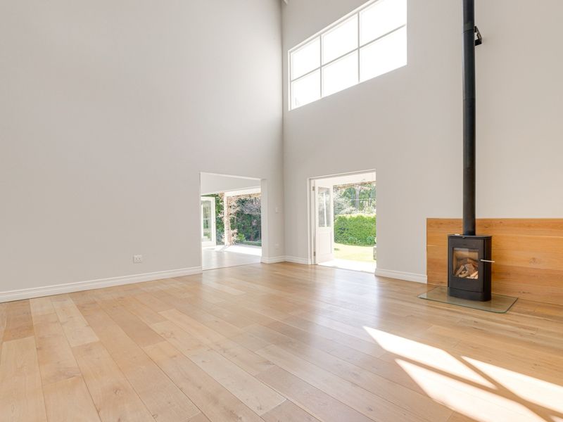 Spacious, light-filled living area featuring high ceilings, timber flooring, and a modern wood-burning fireplace, with direct access to the garden.