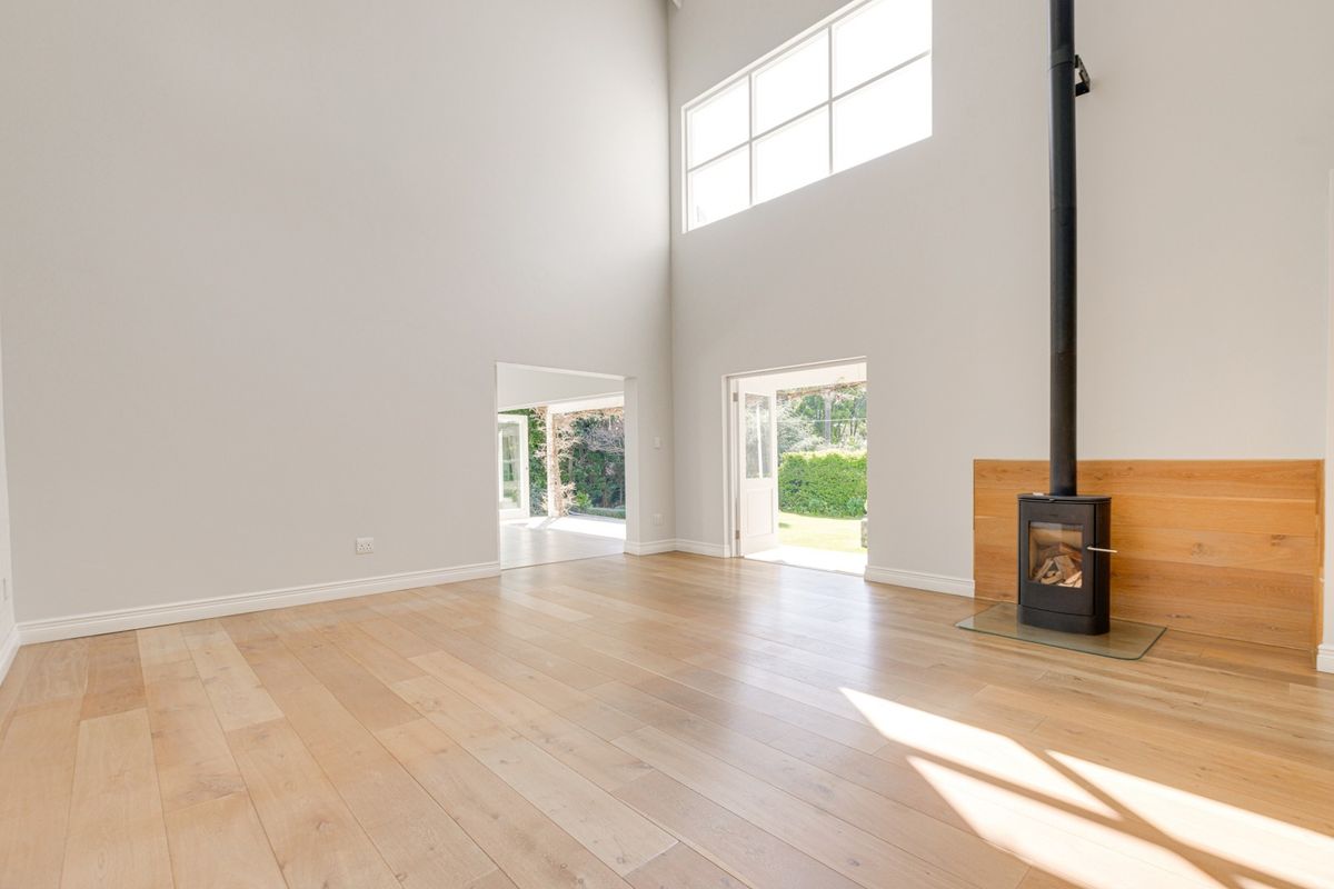 Spacious, light-filled living area featuring high ceilings, timber flooring, and a modern wood-burning fireplace, with direct access to the garden.