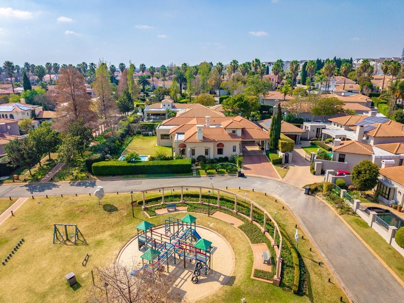 Aerial view of a residential property featuring a terracotta tiled roof, paved driveway, private swimming pool, and well-maintained garden within a suburban estate.