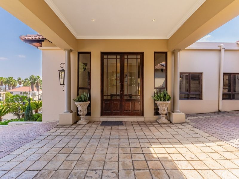 A grand covered entrance featuring a double timber front door with sidelights, stone paving, and elegant architectural columns.