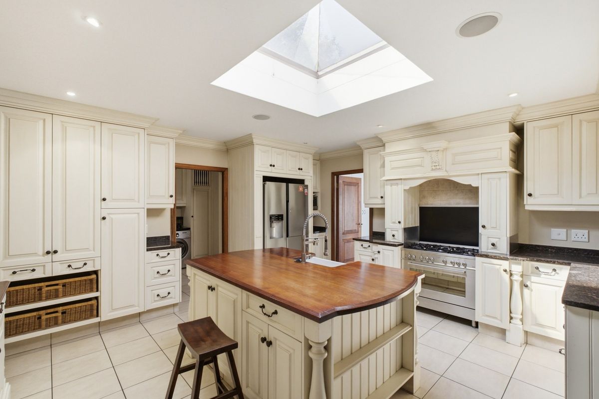 Spacious kitchen featuring a large central island with a wooden countertop, custom cabinetry, a gas range, and a bright skylight overhead.