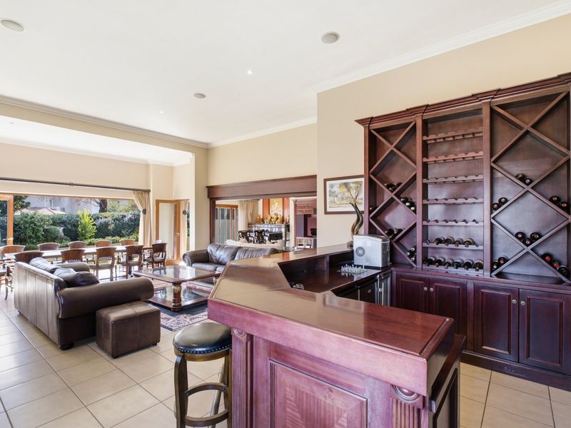 Spacious open-plan living area featuring a custom built-in wooden bar with integrated wine storage, tiled floors, and seamless access to the outdoor patio.