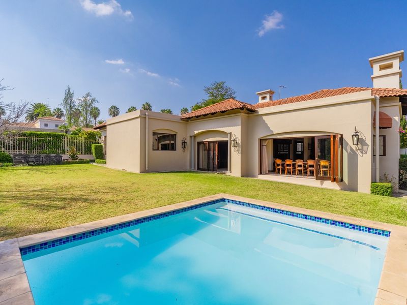 Rear view of the property featuring a swimming pool, landscaped garden, and a covered patio area with bi-fold doors leading into the home.