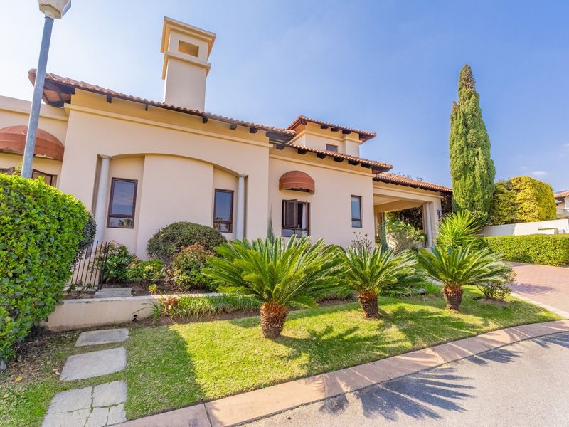 A well-maintained front elevation of a house featuring a tiled roof, chimney, and established landscaped garden with a paved driveway.