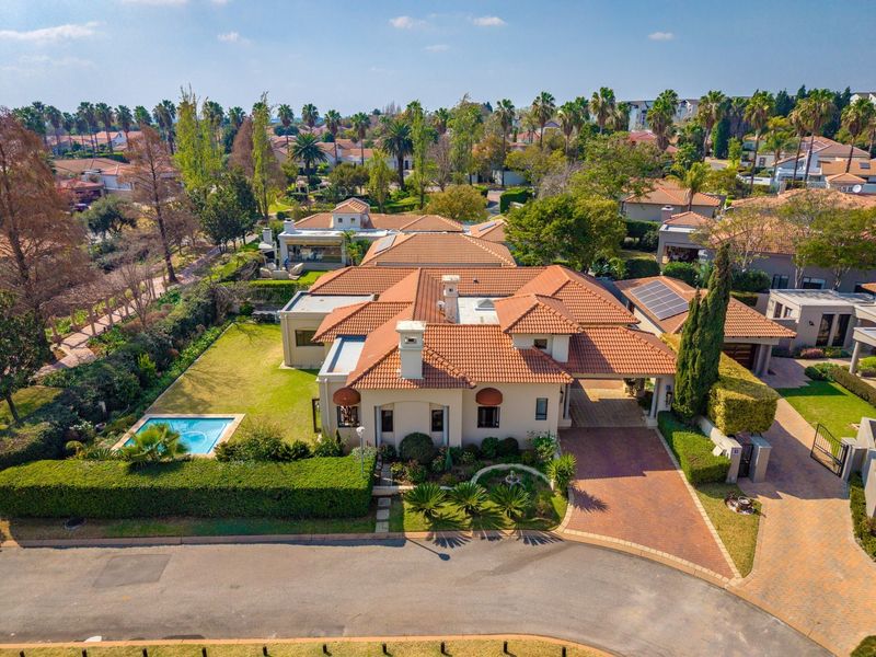 Aerial view of a residential property featuring a terracotta tile roof, private swimming pool, landscaped garden, and a paved driveway with a covered carport.