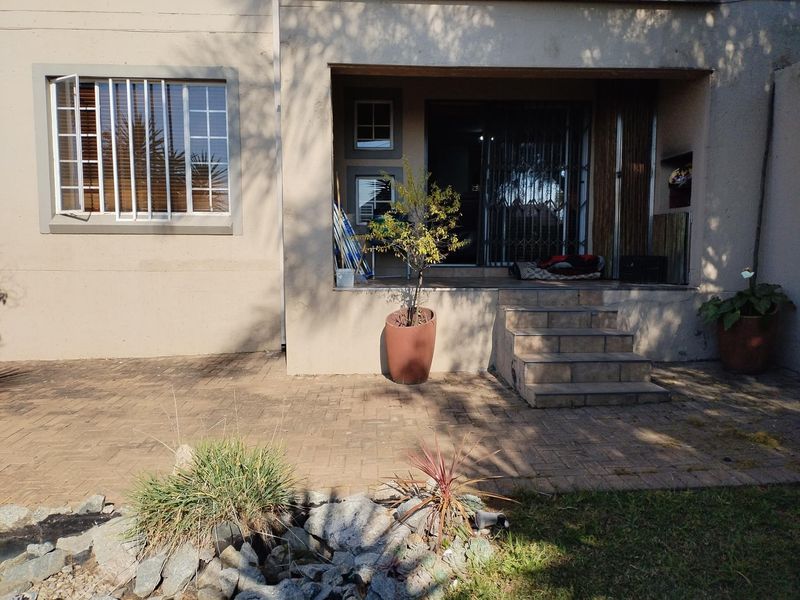 Rear exterior view of the apartment featuring a paved patio area, tiled steps, and secure sliding door access.