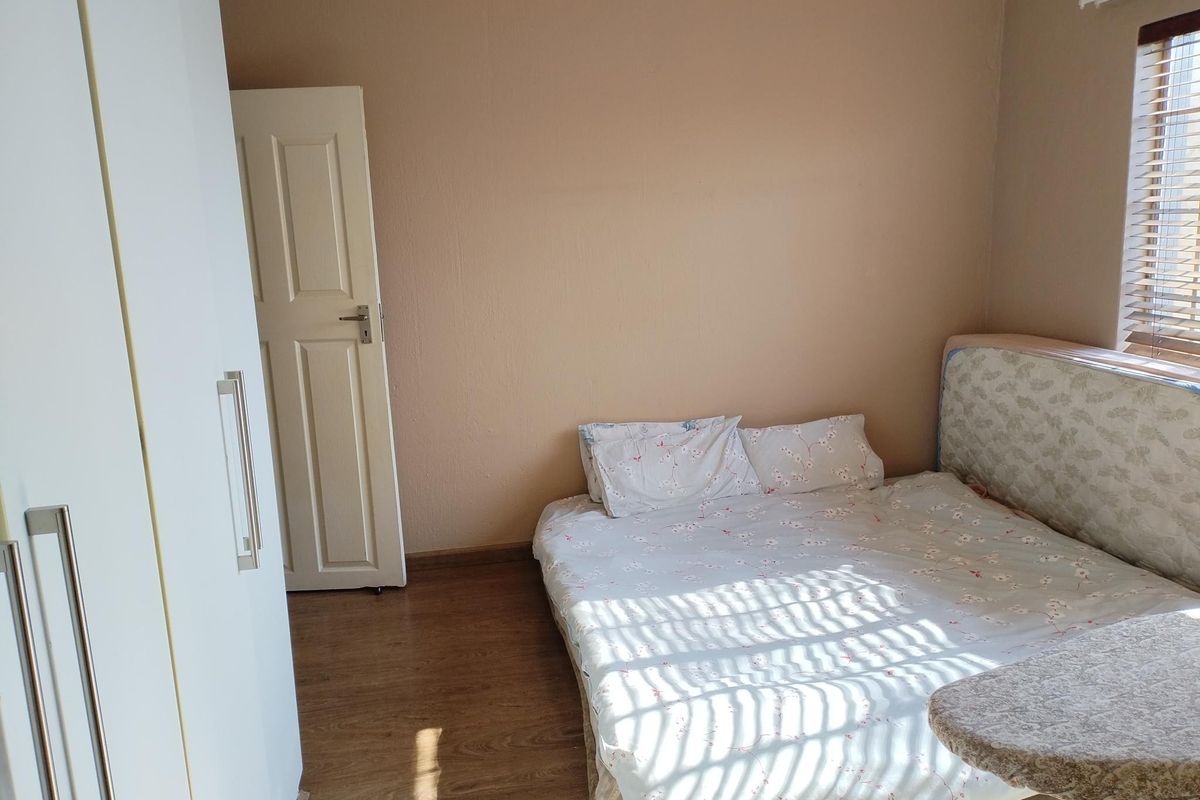 A bedroom featuring laminate flooring, a built-in wardrobe, and venetian blinds, providing a functional space with neutral wall tones.