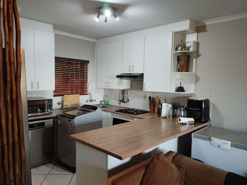 A functional kitchen featuring white cabinetry, a wood-look breakfast bar, gas hob, and integrated laundry space, offering a practical layout for daily living.