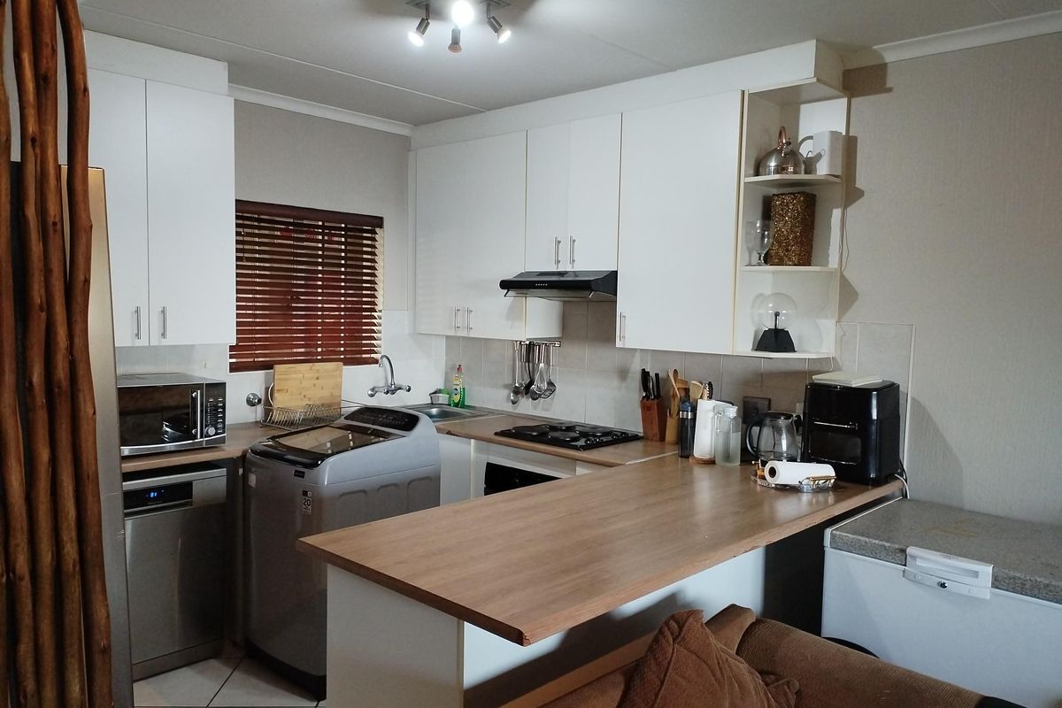 A functional kitchen featuring white cabinetry, a wood-look breakfast bar, gas hob, and integrated laundry space, offering a practical layout for daily living.