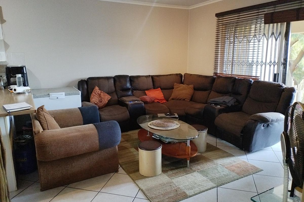 A spacious living room featuring tiled flooring, security gates on the windows, and venetian blinds, offering a functional and comfortable living space.