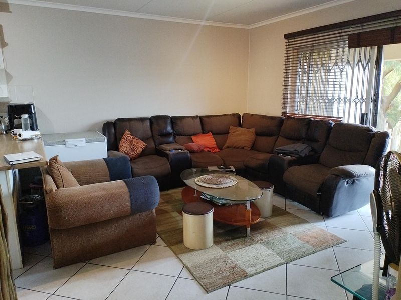 A spacious living room featuring tiled flooring, security gates on the windows, and venetian blinds, offering a functional and comfortable living space.