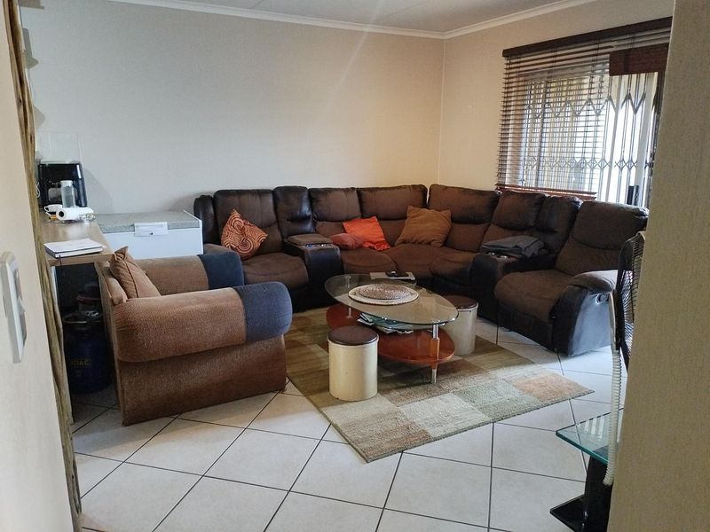 A comfortable living room featuring tiled flooring, large windows with venetian blinds, and a security gate for added peace of mind.