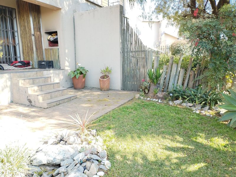 A private rear garden featuring a paved patio area, tiled steps leading to the entrance, and established landscaping with timber fencing.