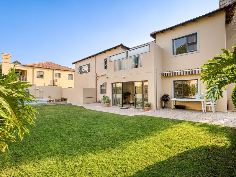 Rear view of the property featuring a paved patio, landscaped garden, swimming pool, and a balcony overlooking the backyard.