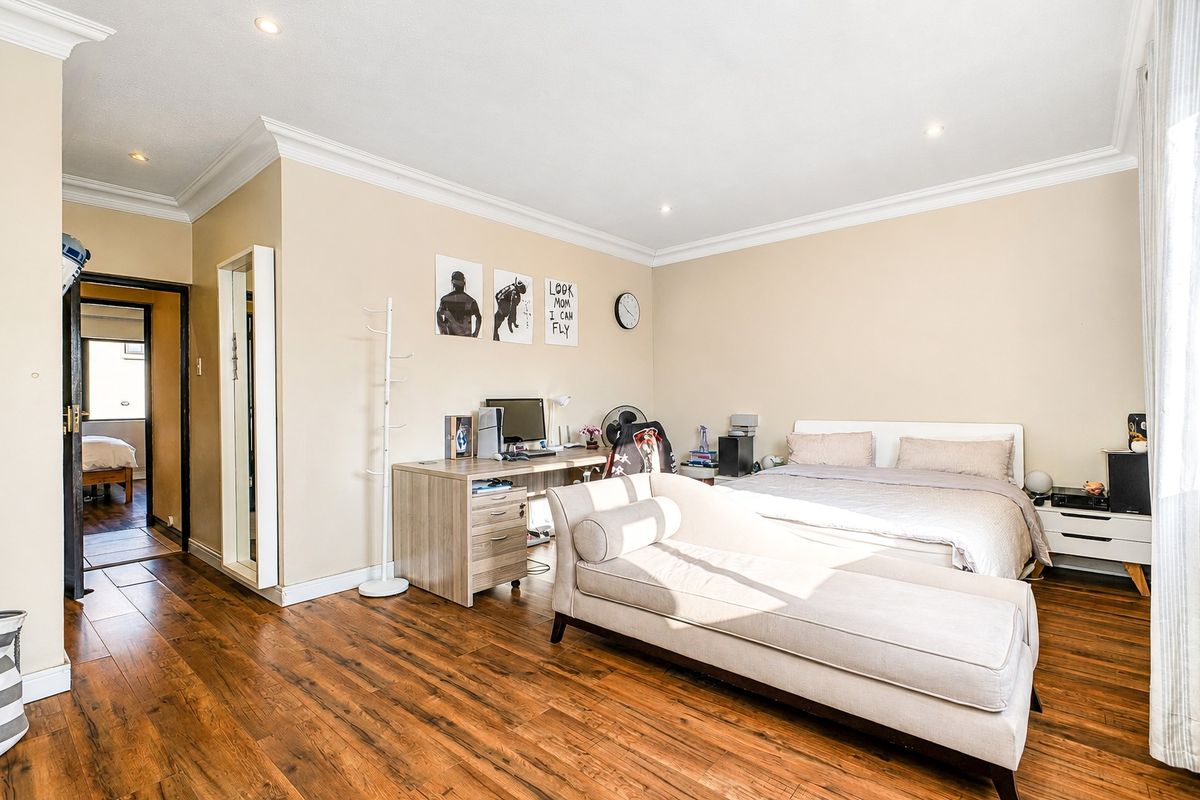 A well-lit bedroom featuring warm-toned laminate flooring, crown molding, and recessed ceiling lighting, offering a comfortable and functional living space.