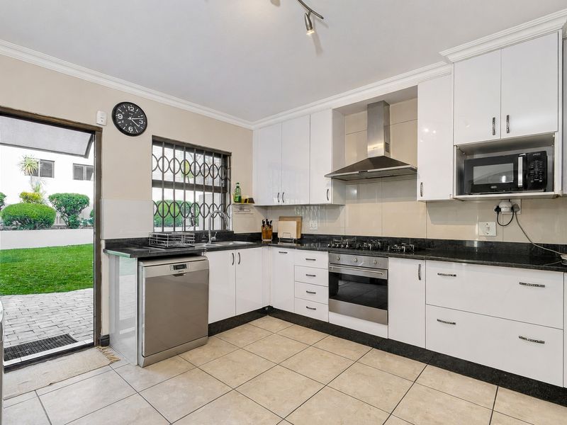Modern kitchen featuring white cabinetry, granite countertops, stainless steel appliances, and direct access to the rear garden through a secure glass door.