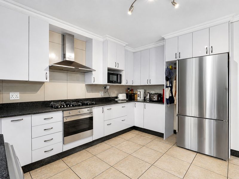 Modern kitchen featuring white cabinetry, granite countertops, gas hob, built-in oven, extractor fan, and tiled flooring.