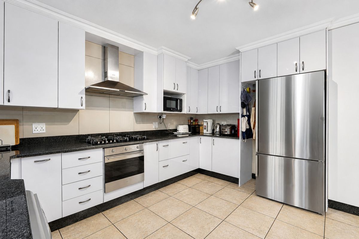 Modern kitchen featuring white cabinetry, granite countertops, gas hob, built-in oven, extractor fan, and tiled flooring.