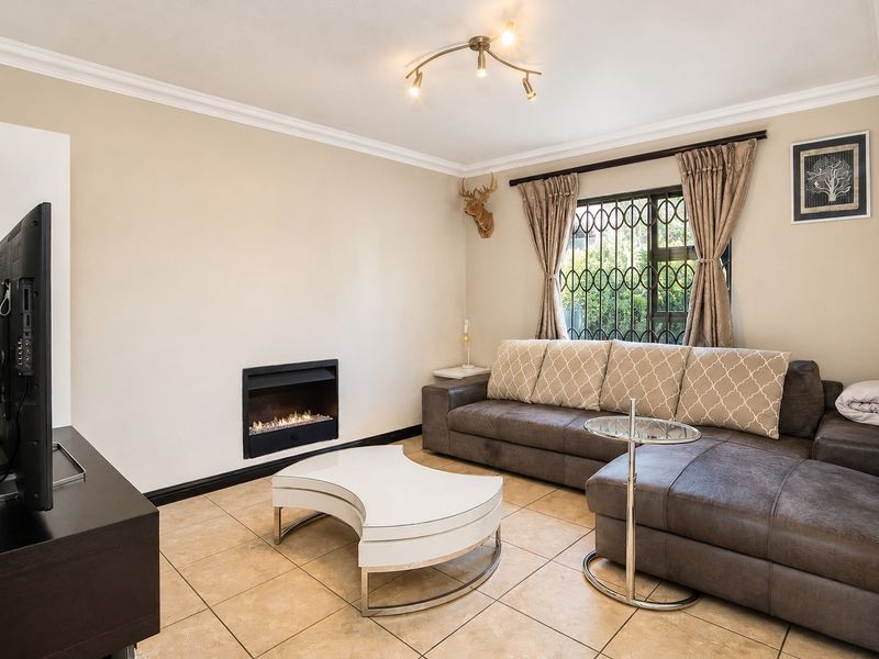 A comfortable living room featuring tiled flooring, a built-in fireplace, and a window fitted with security bars.