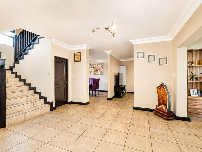 Spacious open-plan living area featuring tiled flooring, a prominent staircase with a wooden balustrade, and built-in shelving units.