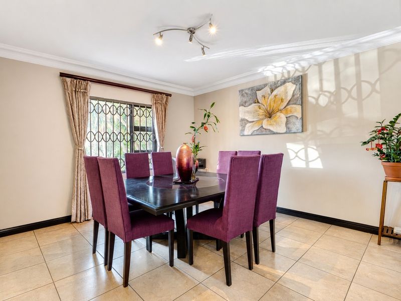 A well-maintained dining room featuring neutral tiled flooring, coved ceilings, and a window fitted with security bars for added peace of mind.