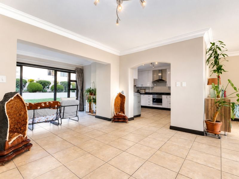 Spacious open-plan living area featuring tiled floors, coved cornicing, and a seamless transition to a modern kitchen with built-in appliances and garden access.