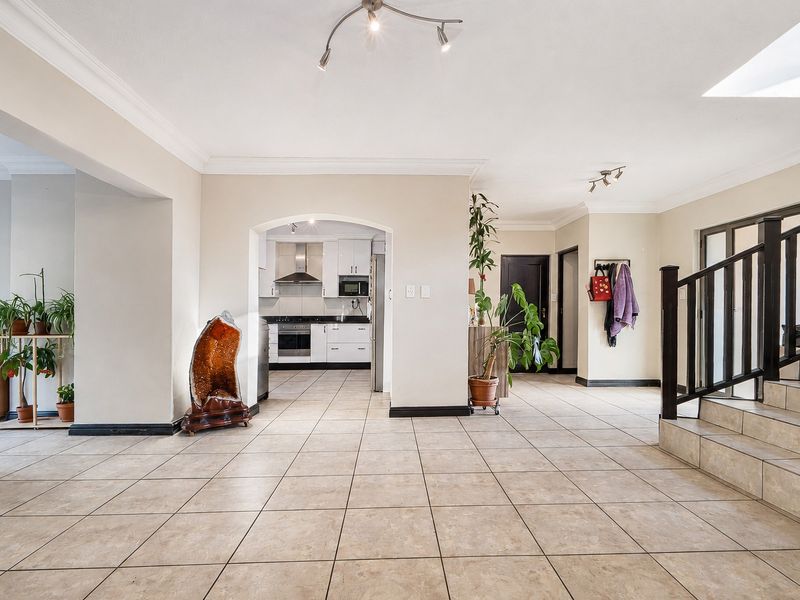 Spacious open-plan living area featuring tiled floors, a central archway leading to a modern kitchen, and a staircase with a wooden balustrade.