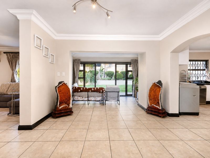 Spacious open-plan living area featuring neutral ceramic floor tiles, crown molding, and large sliding glass doors providing direct access to the garden.