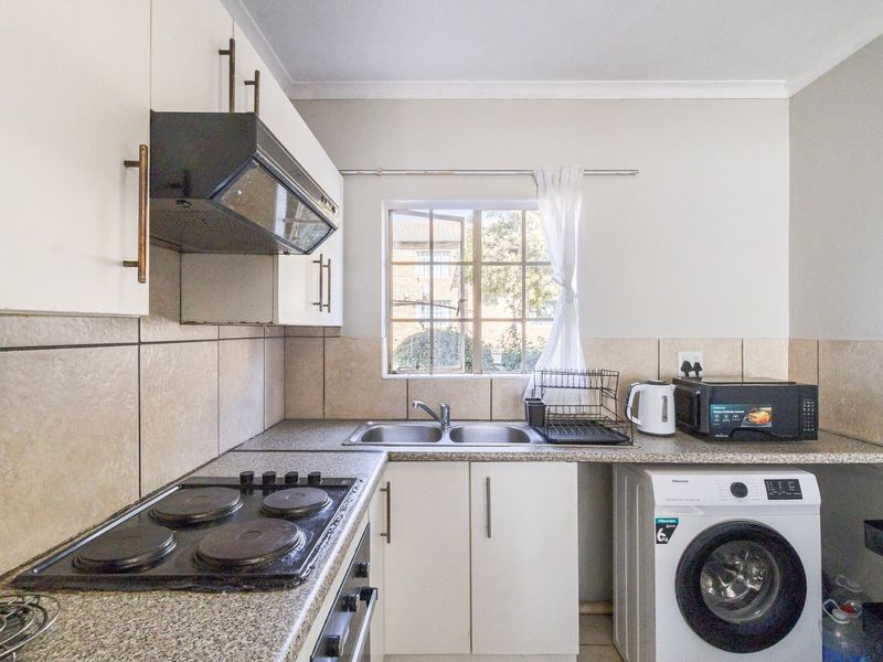 A functional kitchen featuring white cabinetry, laminate countertops, a double sink, built-in electric hob, oven, and extractor fan with tiled splashbacks.