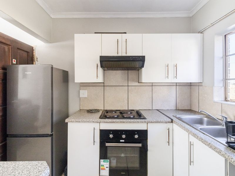 A functional kitchen featuring white cabinetry, granite countertops, a tiled backsplash, and integrated appliances including an oven, hob, and extractor fan.