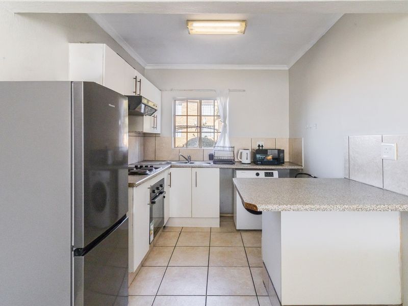 Functional kitchen featuring white cabinetry, laminate countertops, built-in oven with gas hob, tiled backsplash, and a convenient breakfast bar area.
