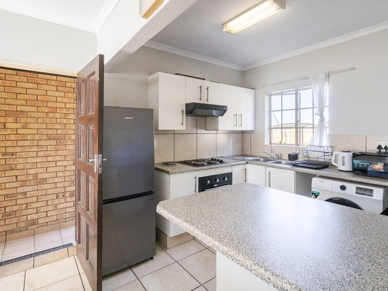 Functional kitchen featuring white cabinetry, laminate countertops, built-in oven and hob, tiled backsplash, and integrated laundry plumbing connections.