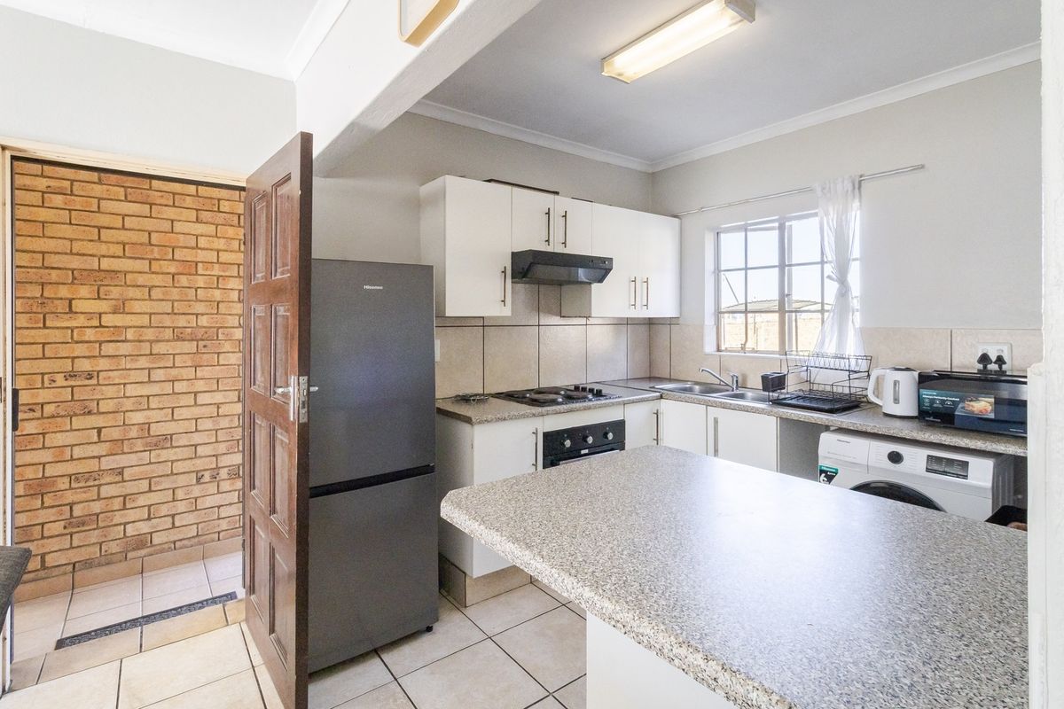 Functional kitchen featuring white cabinetry, laminate countertops, built-in oven and hob, tiled backsplash, and integrated laundry plumbing connections.