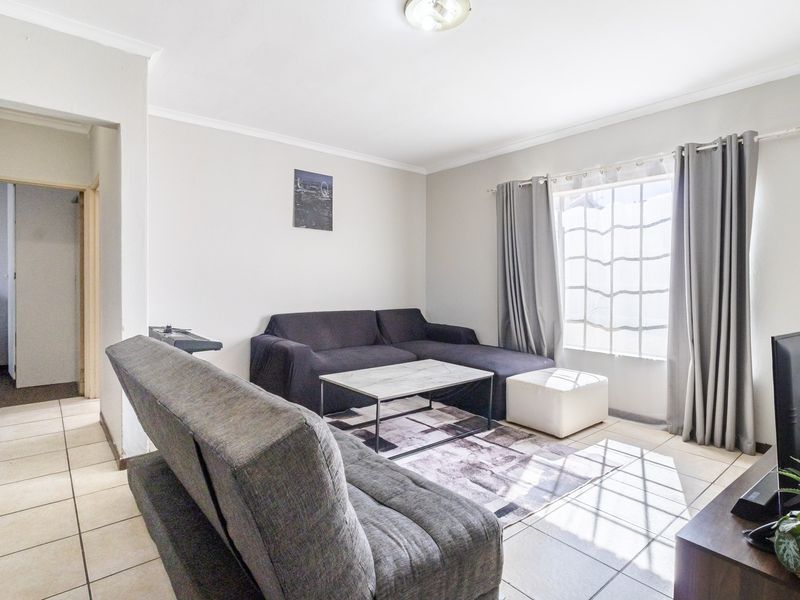 A bright living room featuring neutral tiled flooring, coved ceilings, and natural light through a large window.
