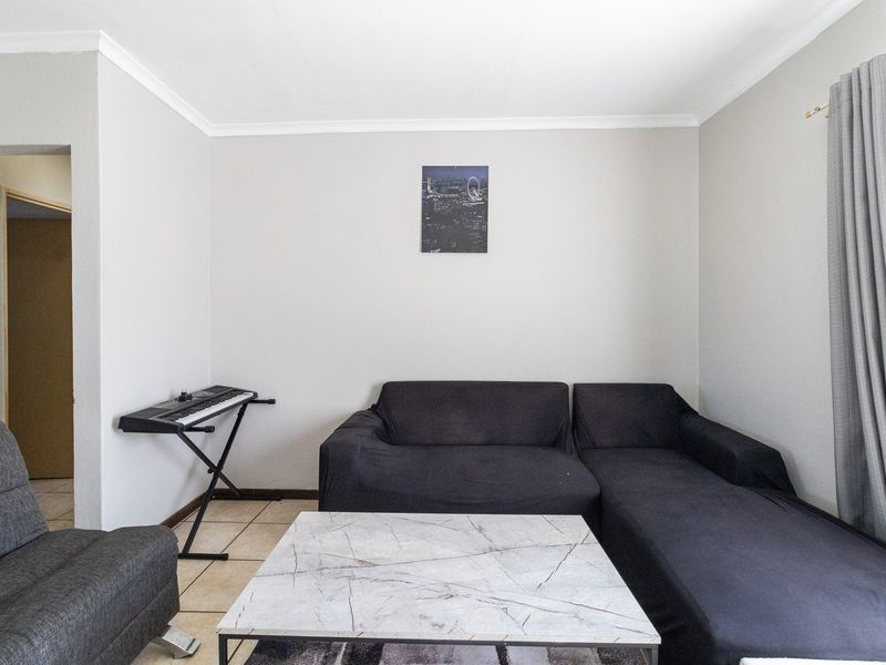 A living room featuring neutral wall finishes, tiled flooring, and decorative cove cornicing, providing a functional and well-lit space.