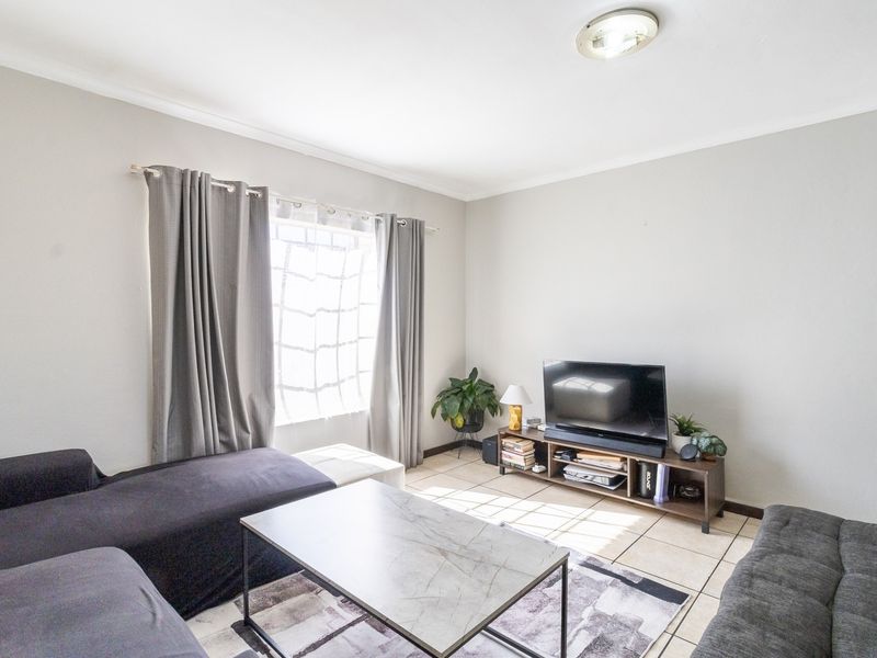 A bright living room featuring neutral wall tones, tiled flooring, and a large window with curtain treatments.