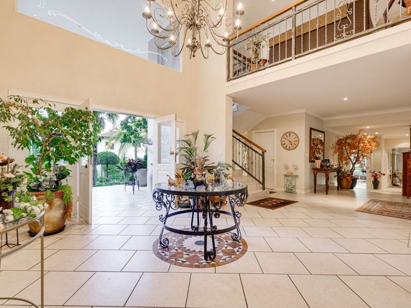 Spacious double-volume entrance hall featuring a grand chandelier, tiled flooring, and an open mezzanine landing overlooking the foyer.