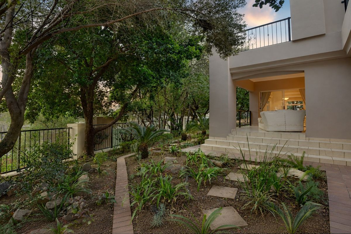 A rear exterior view featuring a tiled patio, landscaped garden with mature trees, and a wrought iron balcony overlooking the outdoor space.