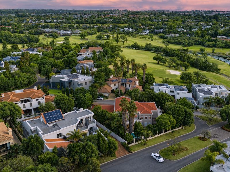 An elevated aerial view of a residential estate featuring multiple homes with solar installations, tiled roofs, and proximity to a golf course.