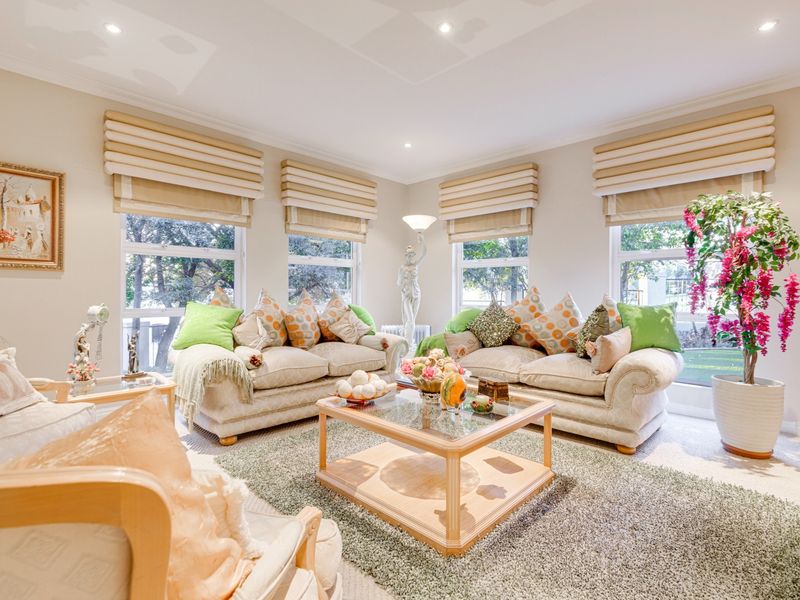 A bright and spacious living room featuring large windows with fitted roman blinds, recessed downlighting, and elegant coved cornicing.
