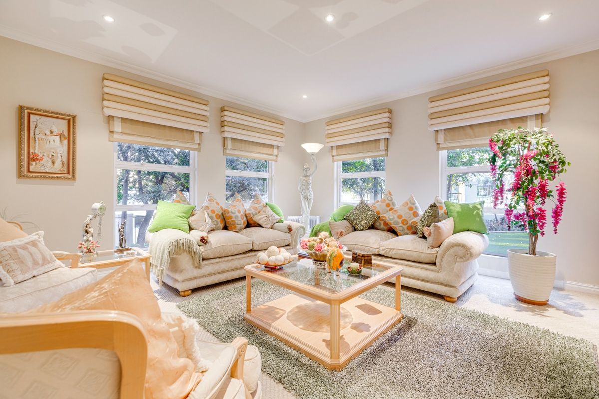 A bright and spacious living room featuring large windows with fitted roman blinds, recessed downlighting, and elegant coved cornicing.