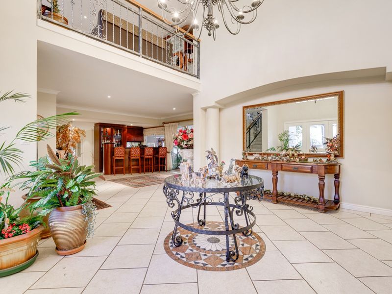 Spacious double-volume entrance hall featuring elegant tiled flooring, a grand chandelier, and a mezzanine overlook, leading into an open-plan living and bar area.
