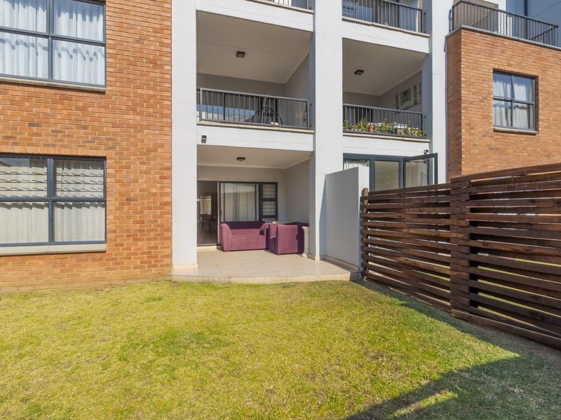 Rear view of an apartment building featuring a ground-floor tiled patio, a small private lawn, and a timber privacy screen.