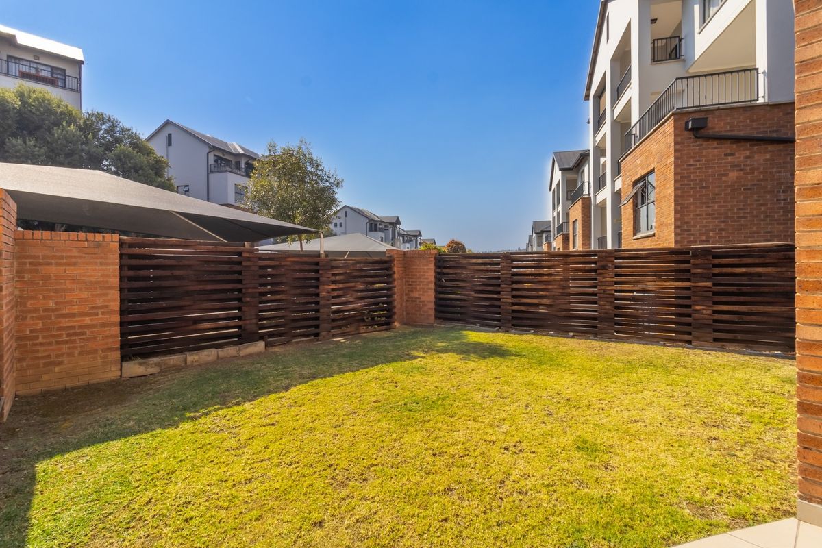A private rear garden area featuring a well-maintained lawn, brick boundary walls, and timber slat fencing within an apartment complex.